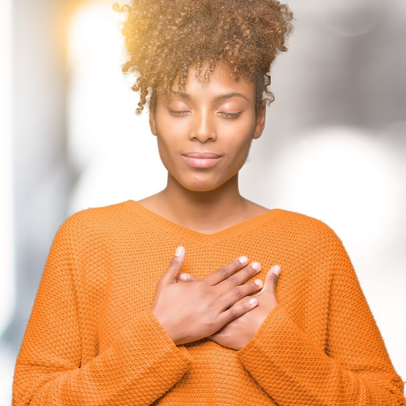 woman with eyes closed, hands over heart. looking peaceful