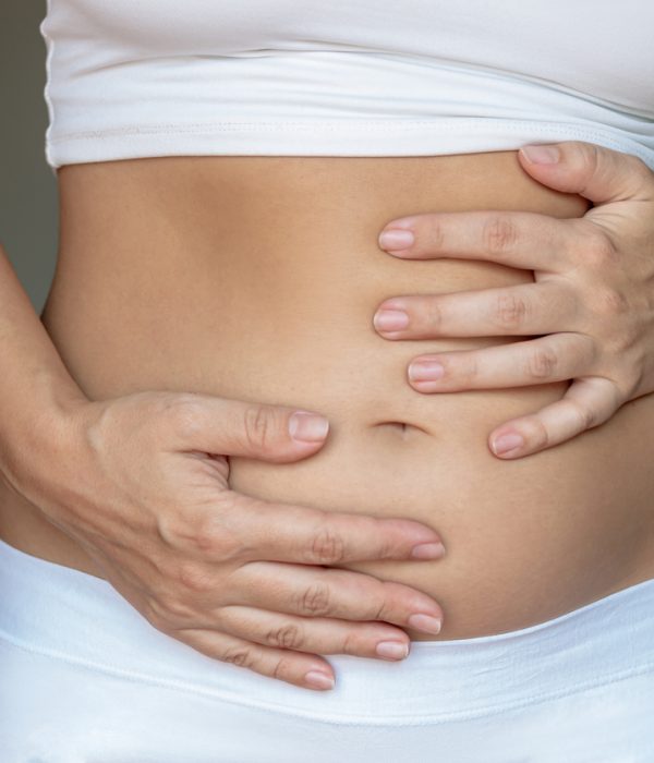 Stomach ache, bloating, flatulence, abdominal distension, colic, digestive disorders. Young woman holding her stomach with her hands Stomach ache, bloating, flatulence, abdominal distension, colic, digestive disorders. A young woman holding her stomach with her hands on a dark gray background. Overeating, overweight, excess weight