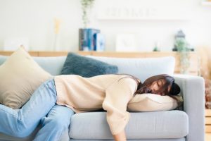 Asian woman resting at home on couch, feeling exhausted after work, lacking energy, or overworked, too tired, and lacking motivation